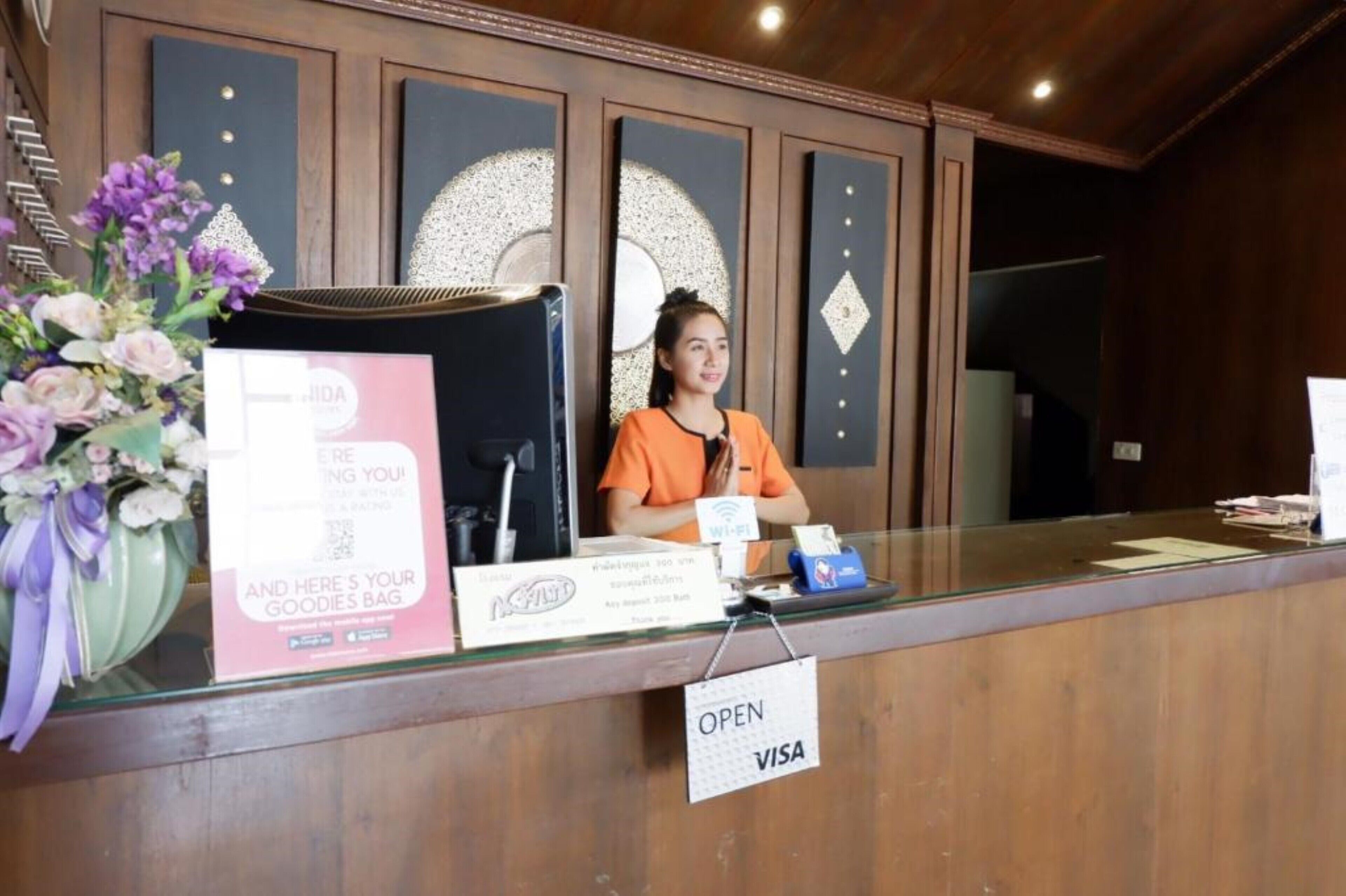 Un mostrador de recepción con un letrero que indica 'ABIERTO' y 'VISA' para pagos con tarjeta. Se ve un arreglo floral a la izquierda.