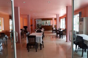 A spacious dining area with multiple tables and chairs, a central counter, and large windows allowing natural light. - Na Chaidej Hotel (Surat Thani)