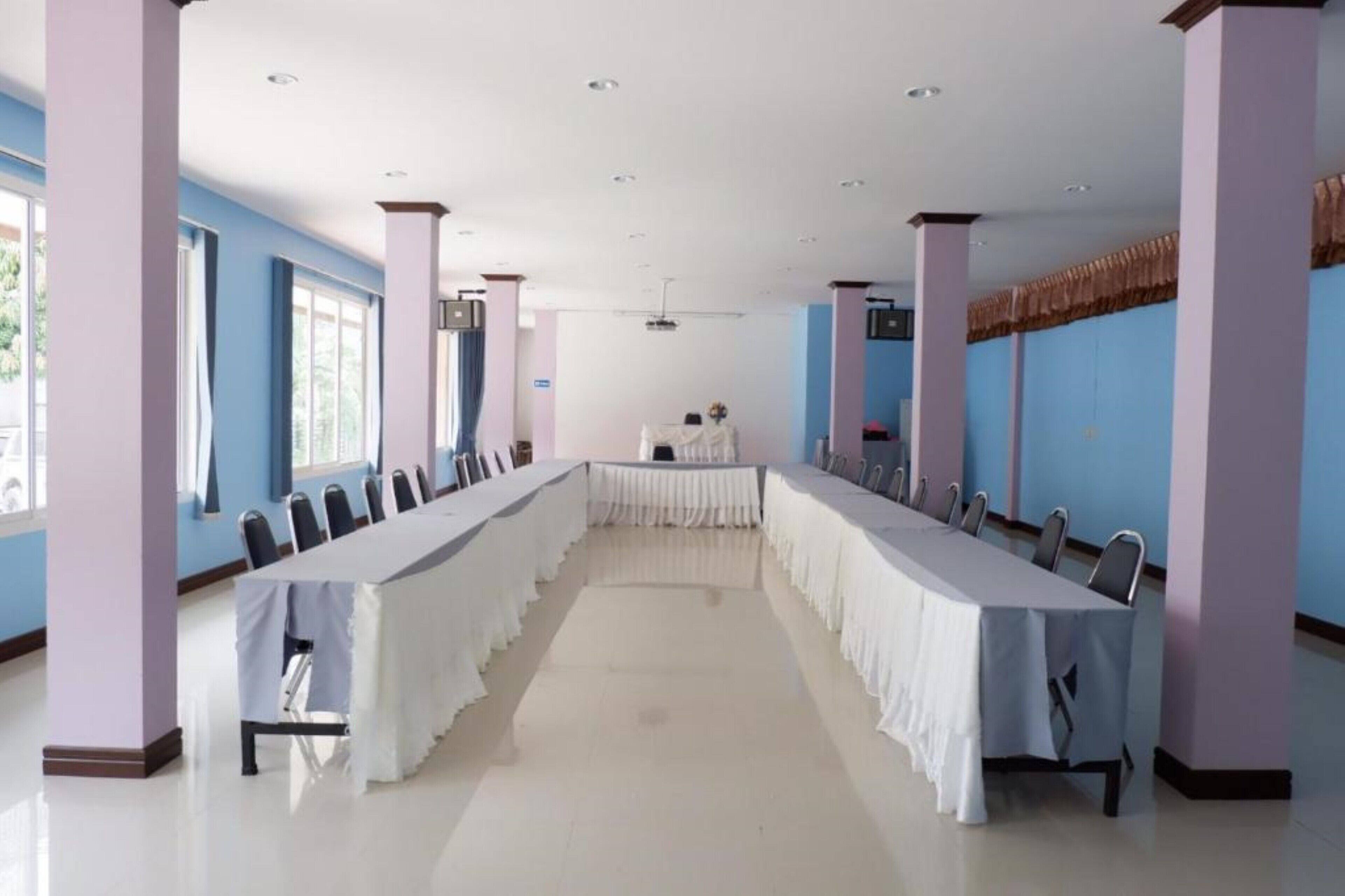 Uma sala de conferência com uma mesa comprida e cadeiras, janelas amplas e um ventilador de teto.