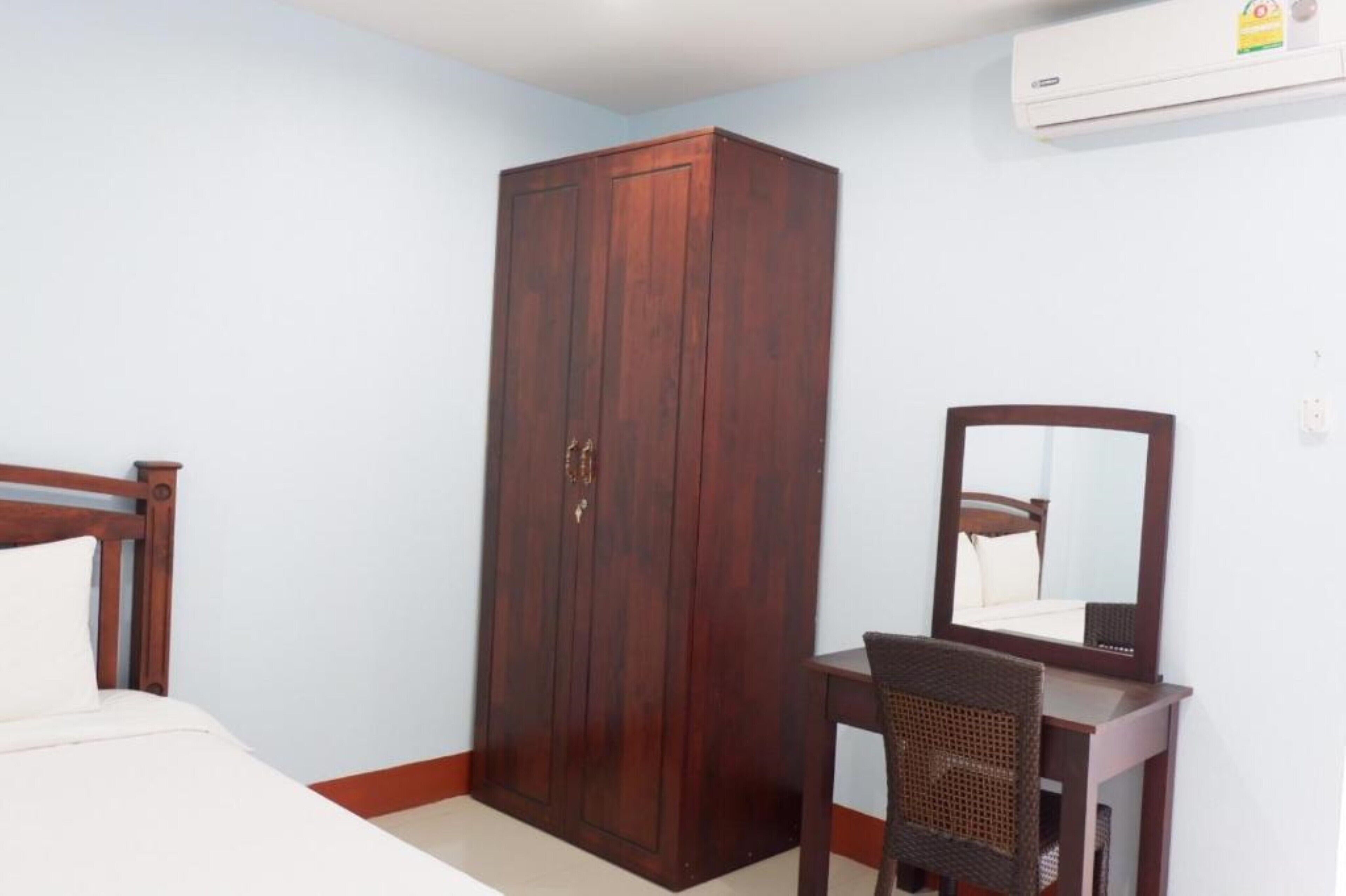A bedroom with a wooden wardrobe, a bed, a desk with a chair, and a mirror.