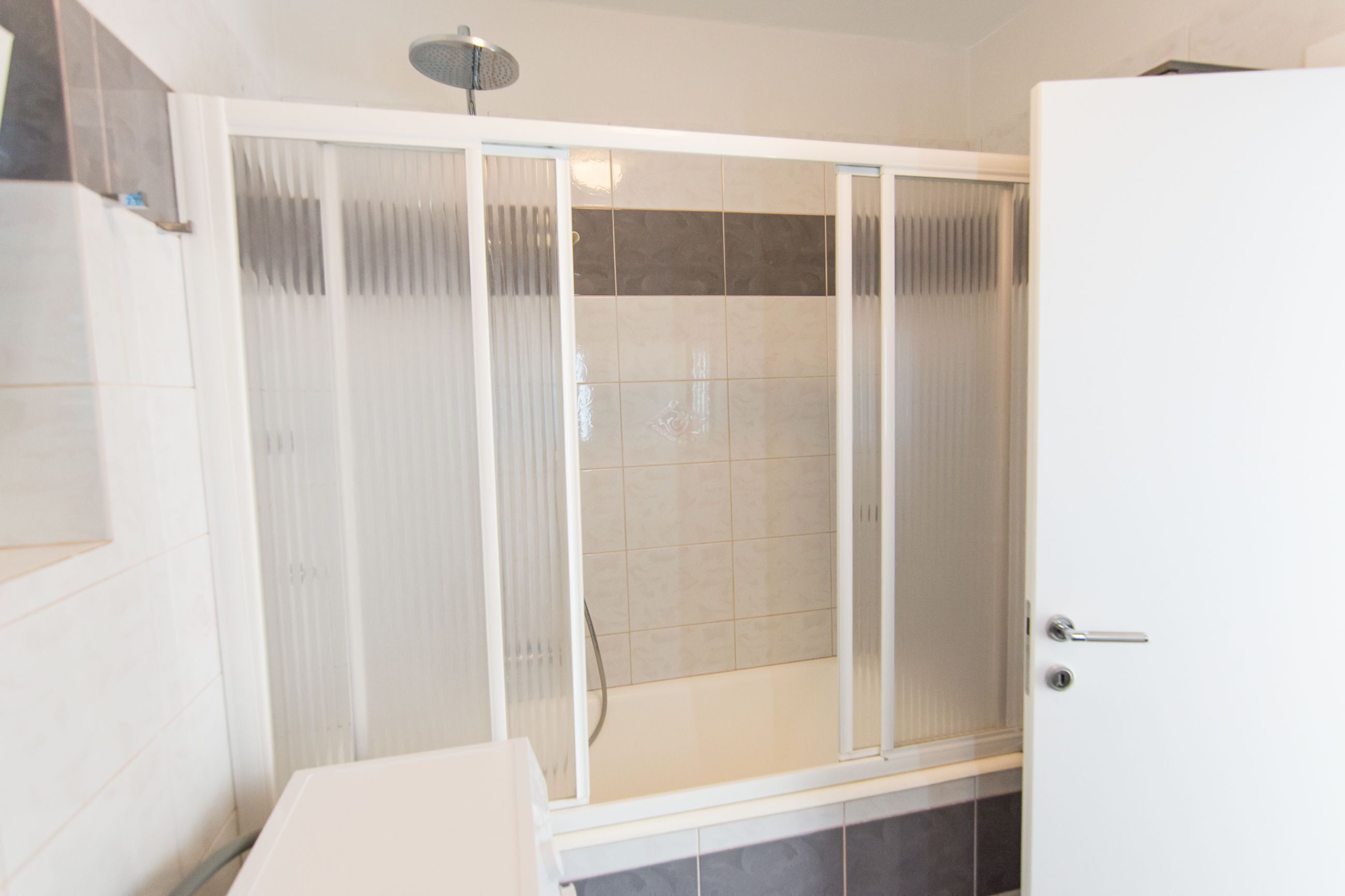 A shower enclosure with frosted glass doors, a tiled shower area, and a white door with a handle.