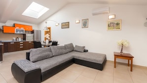 Uma sala de estar moderna com sofá seccional, área de jantar e cozinha com armários laranja.