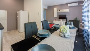 A modern kitchen with a refrigerator, microwave, and stove. There is a dining area with a table set for two, featuring blue plates and a striped vase with flowers. - Apartments Arijana (Dramalj)