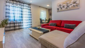 A modern living room with a red sofa, a beige sofa, a coffee table, and a dining area in the background. - Apartments Arijana (Dramalj)