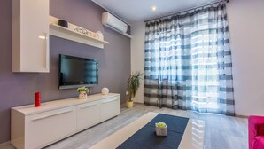 A modern living room with a flat-screen TV, a white cabinet, a potted plant, and a striped curtain. - Apartments Arijana (Dramalj)