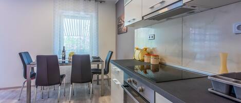 Una cocina moderna con comedor, que incluye una mesa con sillas, un ventanal con cortinas y una estufa.