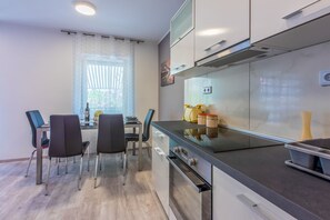 A modern kitchen with a dining area, featuring a table with chairs, a window with curtains, and a stove.