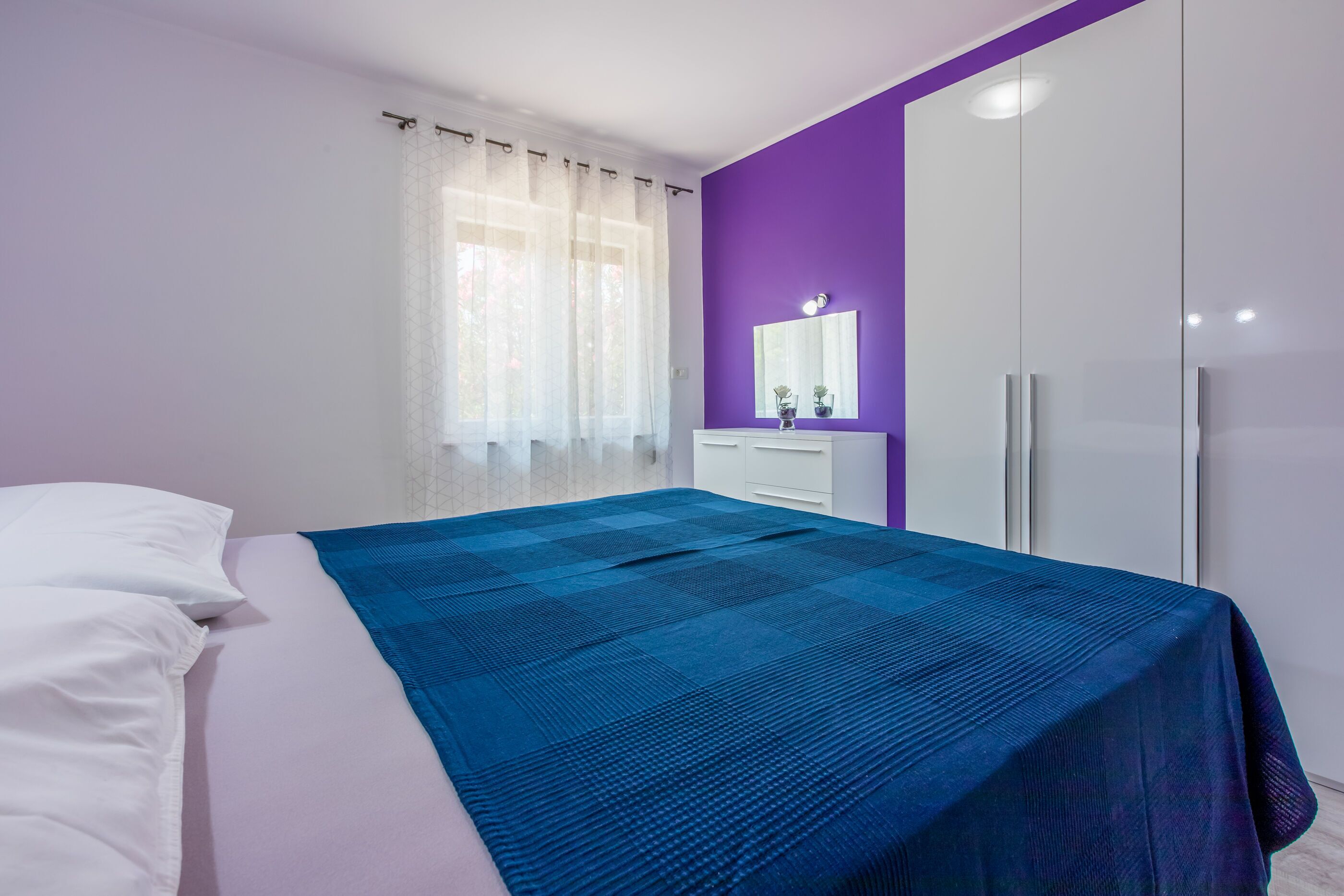 A bedroom with a bed, a dresser, a mirror, and a wardrobe.