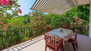 A balcony with a table and chairs, surrounded by a metal railing and lush greenery. - Apartments Arijana (Dramalj)