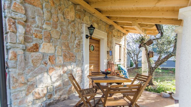 Un patio cubierto con paredes de piedra, mobiliario de madera y vistas del entorno.