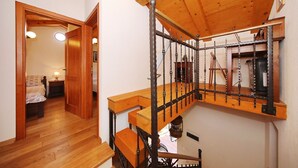 Una escalera de madera con barandilla de metal, techo de madera y una cama en la habitación contigua.