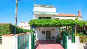 A two-story building with a red-tiled roof, a green gate, and a paved entrance. - Apartment Bilberry (Biograd)