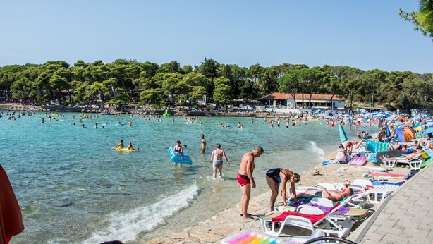 A beach with clear waters, people swimming and sunbathing, and a line of beach chairs and umbrellas. - Apartment Bilberry (Biograd)