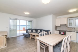 Eine moderne Küche mit Essbereich, ein graues Sofa mit gemusterten Kissen und Blick durch Glastüren.