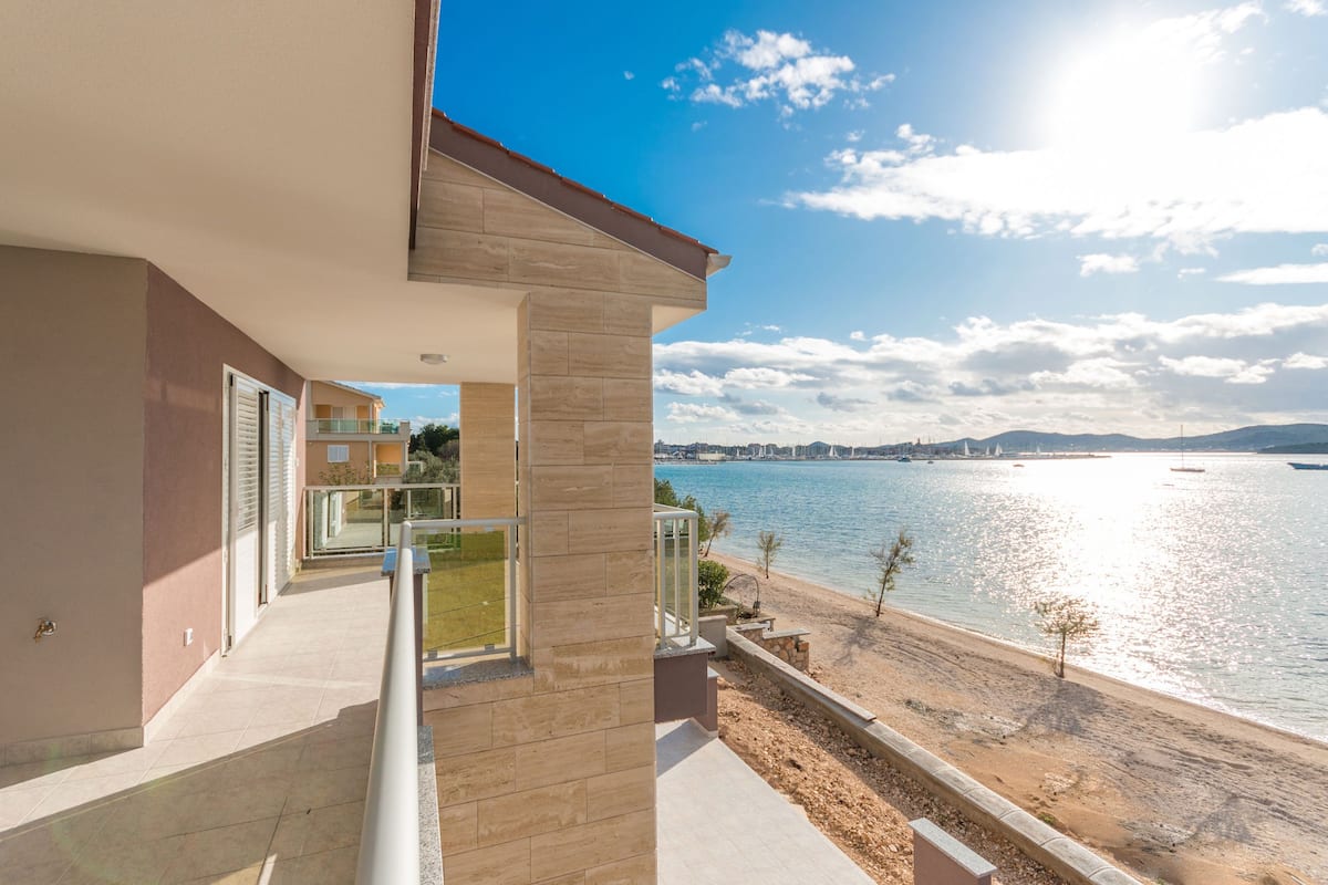 A modern apartment with a balcony overlooking a beach and a body of water.