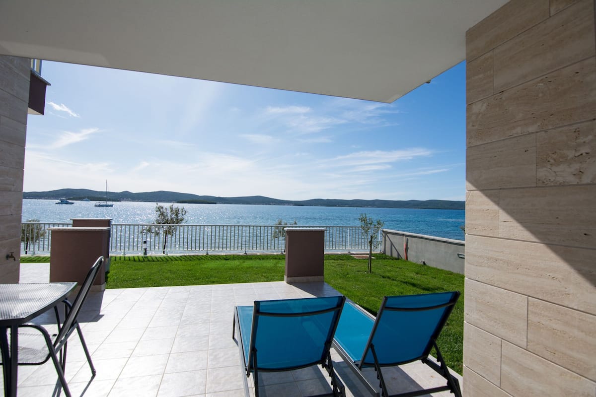 A patio with a view of the sea, a pool, and a table with chairs.