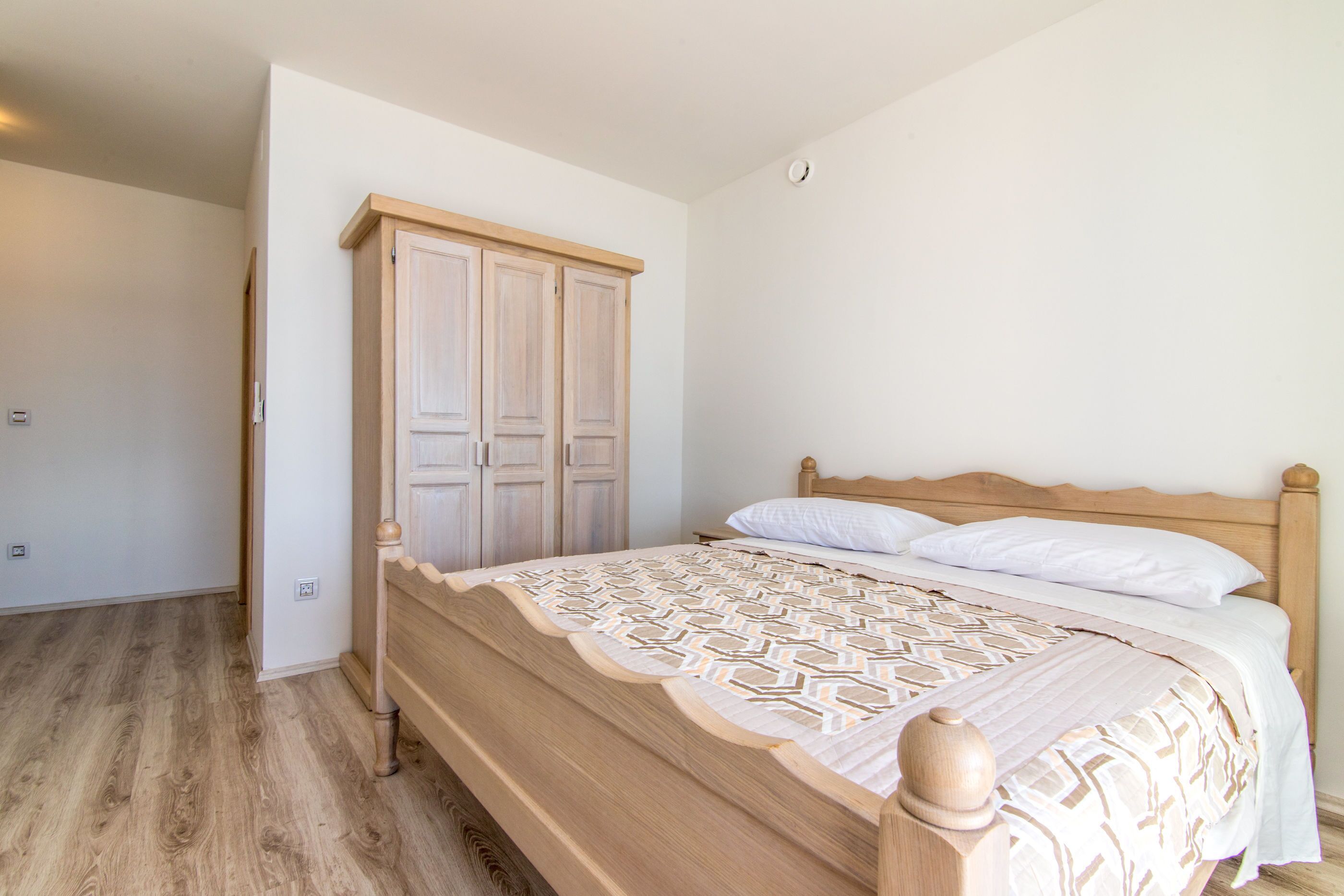 Une chambre à coucher avec un lit en bois, une armoire et un mur blanc uni.
