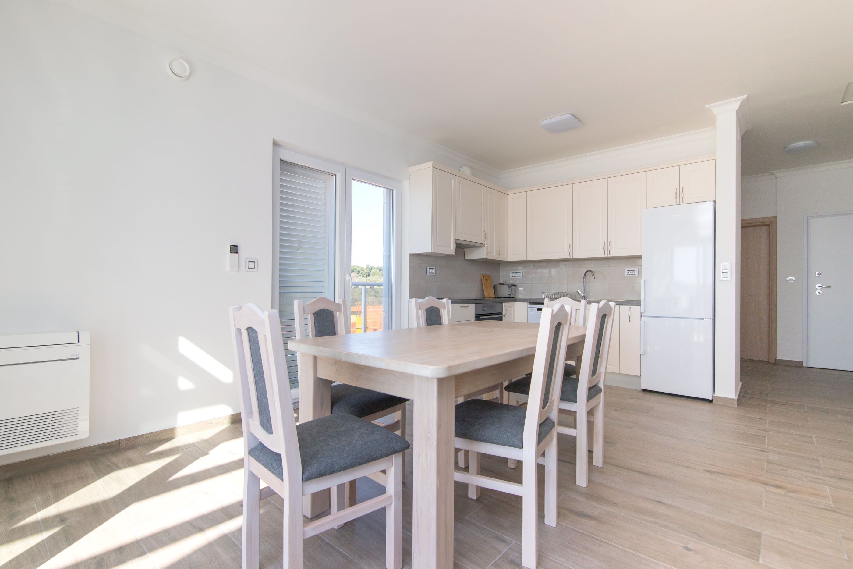 A modern kitchen with white cabinets, a central island, and a dining area with four chairs.