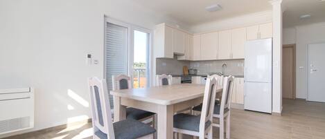 A modern kitchen with white cabinets, a central island, and a dining area with four chairs.