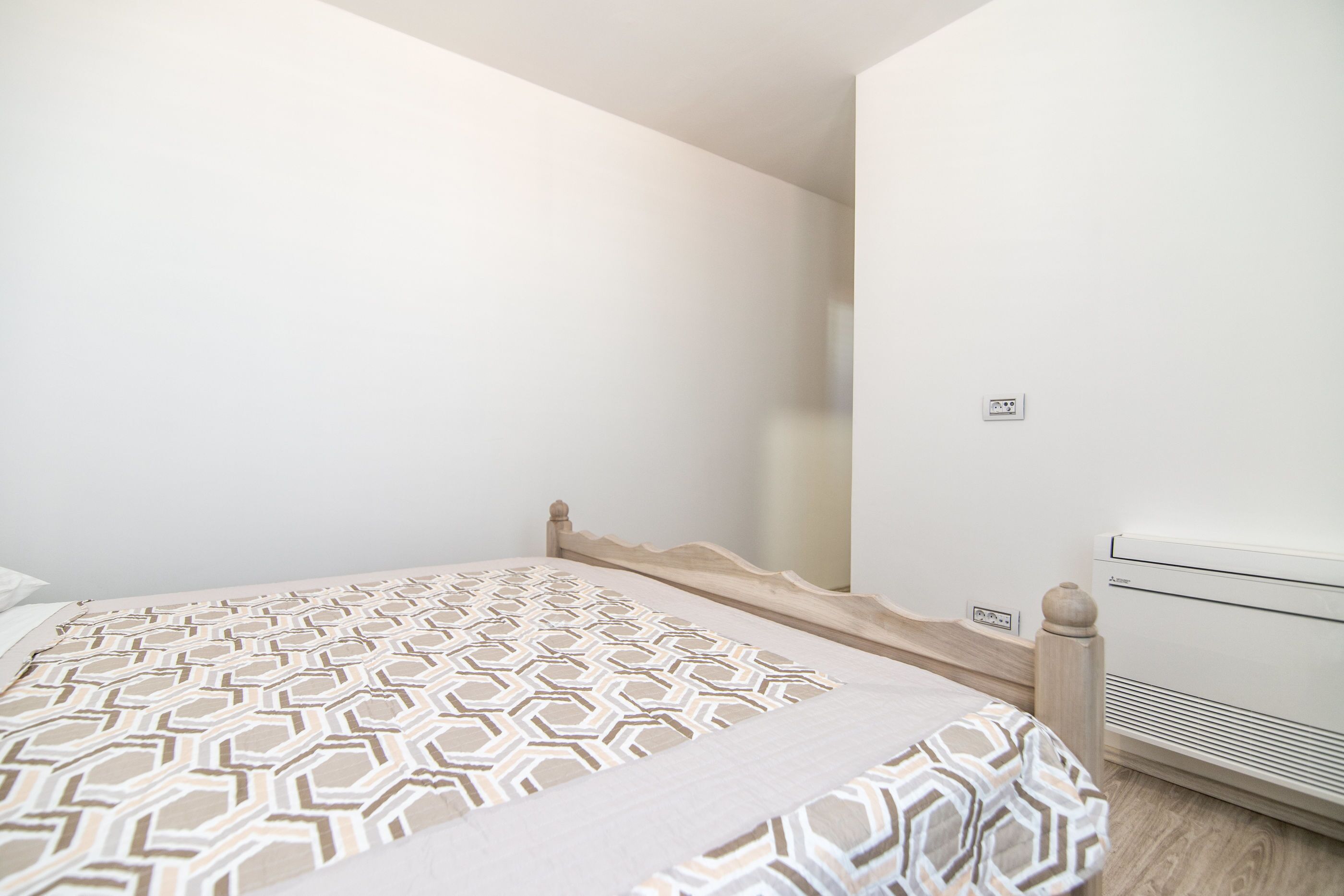 A bedroom with a bed, a wall-mounted air conditioner, and a power outlet.