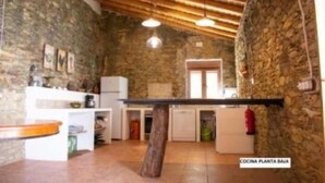 A rustic kitchen with stone walls, wooden beams, and basic amenities including a sink, stove, and refrigerator. - La Casa Grande de Adolfo (La Codosera)