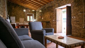 A cozy living room with stone walls, wooden beams, a sofa, armchairs, and a dining table. - La Casa Grande de Adolfo (La Codosera)