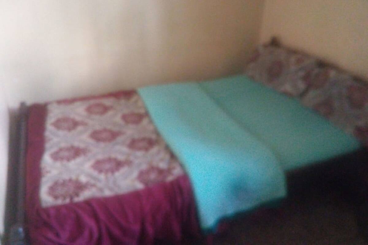 A small, dimly lit room with a single bed featuring a patterned bedspread and a teal blanket.