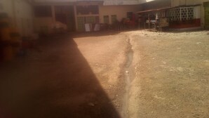 A courtyard with a dirt ground, a building with a sign that reads "FUNCTION GUEST HOUSE," and a covered area with tables and chairs.