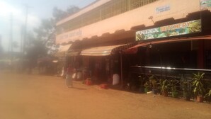 A guesthouse with a dirt road in front, a sign for a butcher shop, and potted plants along the sidewalk.