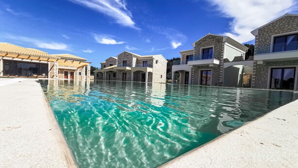 Une piscine avec une façade en pierre et un ciel d’un bleu limpide.