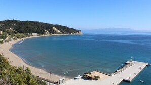 Une plage côtière avec une jetée, une eau d’un bleu limpide et un paysage vallonné en arrière-plan.