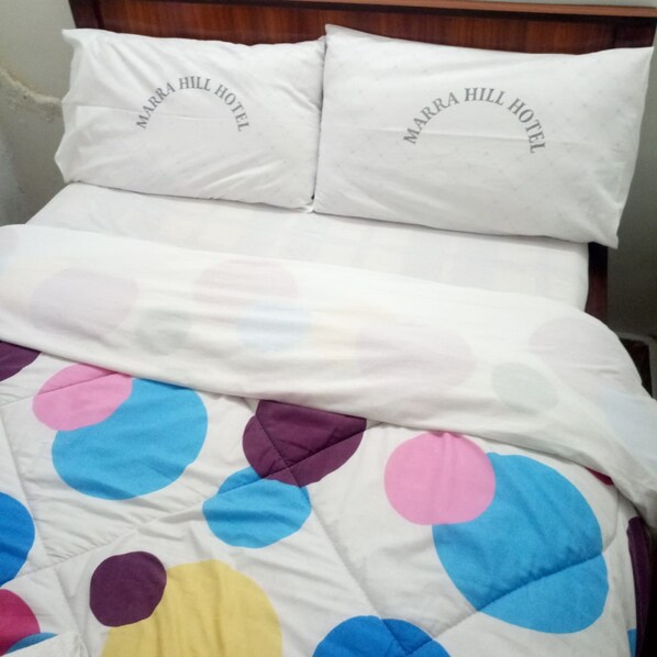 A bed with a white bedspread featuring colorful polka dots and two pillows with the text "MARRA HILL HOTEL". - Marra Hill Hotel (Nakuru)