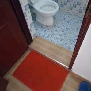 A bathroom with a white toilet, blue and white patterned tiles, a wooden floor, and a red mat. - Marra Hill Hotel (Nakuru)