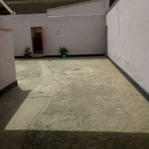 A courtyard with a concrete floor, two potted plants, a door, and a wall with a sign. - Marra Hill Hotel (Nakuru)