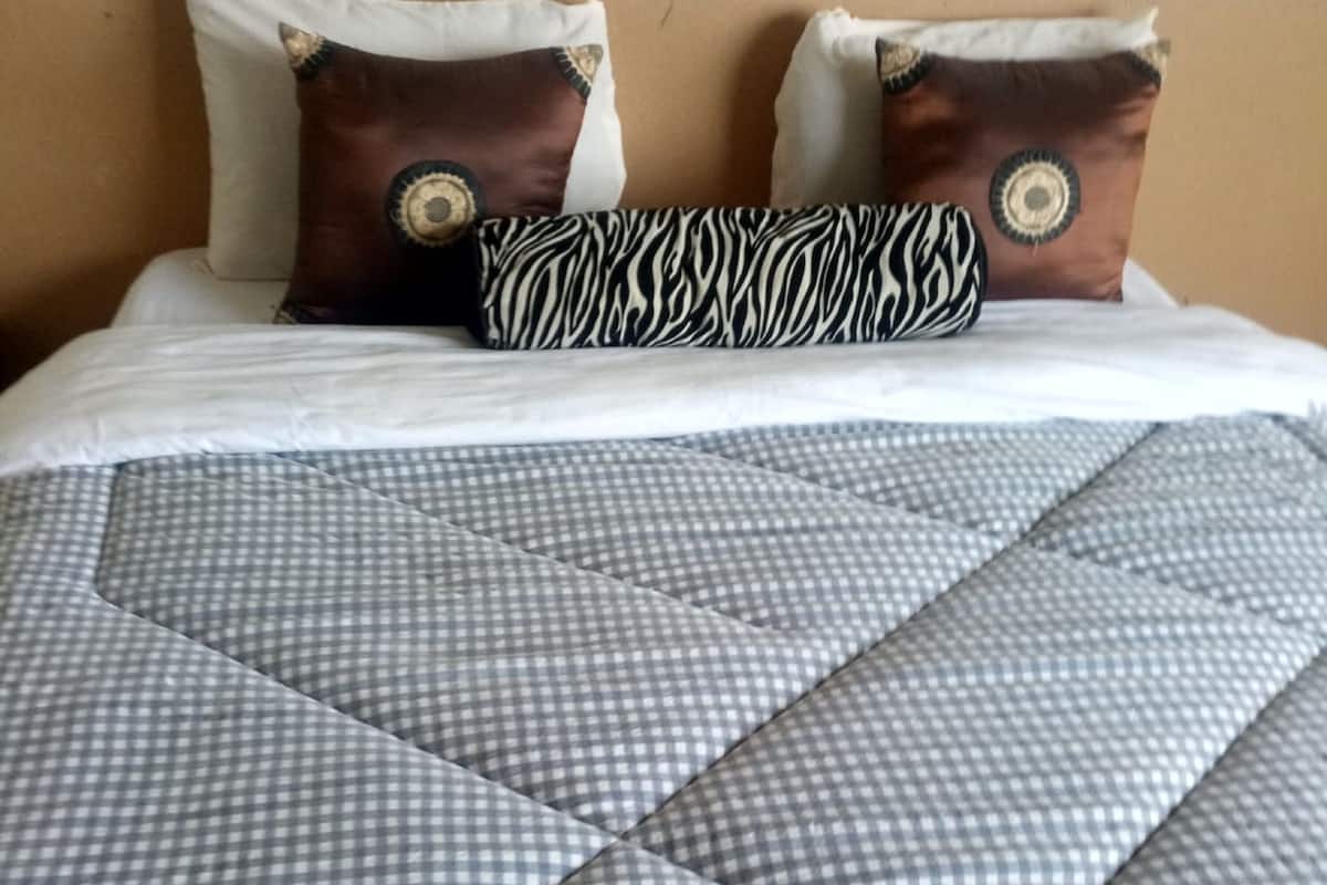 A bed with a checkered duvet cover, two pillows with circular designs, and a blue blanket at the foot of the bed.