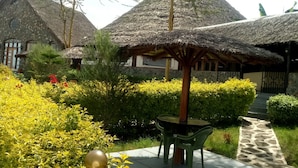 A courtyard with thatched-roof structures, a paved walkway, and well-maintained greenery. - Oldonyo Lodge (Nakuru)
