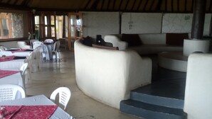 A restaurant with white plastic chairs and tables, a curved white sofa, and a staircase leading to a higher level. - Oldonyo Lodge (Nakuru)