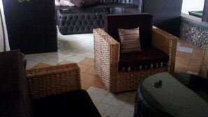 A living area with a black sofa, wicker furniture, and a tiled floor. - Oldonyo Lodge (Nakuru)