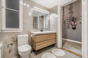 A modern bathroom with a toilet, vanity, mirror, and tiled walls. - Knights Seven Apartment (Budapest)
