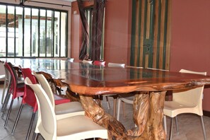 A dining area with a large wooden table surrounded by chairs, large windows, and a door with vertical stripes. - Olerai Hotel (Kitengela)