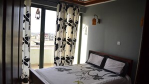 A bedroom with a bed, curtains, and a view of the outside. - Olerai Hotel (Kitengela)