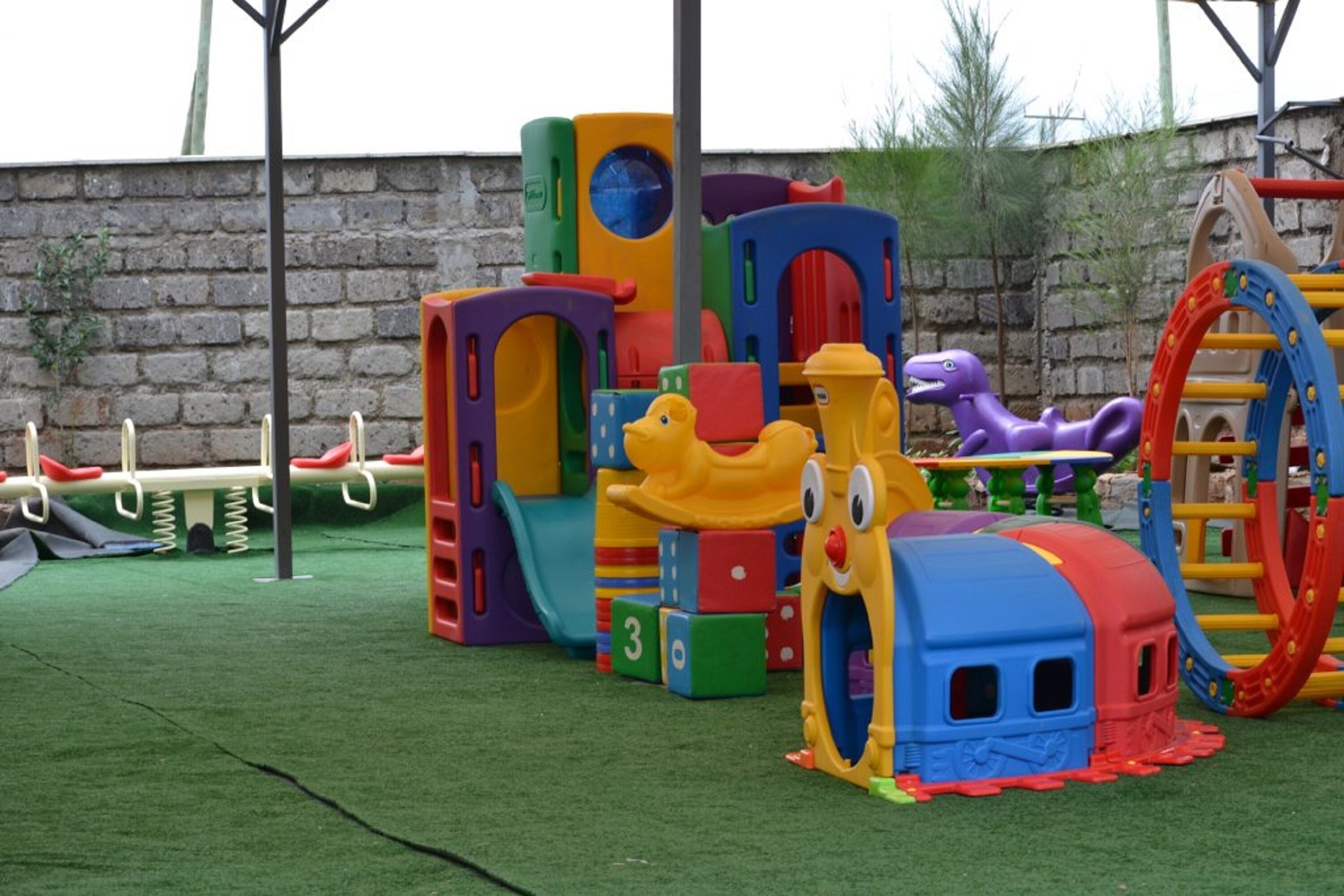 Un área de juegos infantiles con diversas estructuras de colores, que incluyen un tobogán, pared de escalar y un conjunto de juegos con temática de tren.