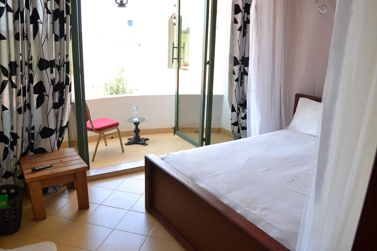 Une chambre à coucher avec un lit, une petite table, une chaise et une fenêtre avec des rideaux.