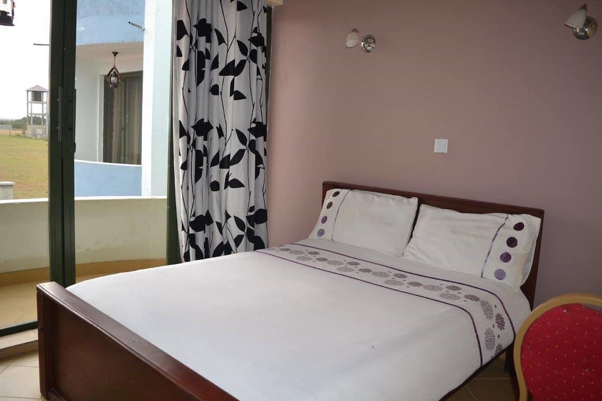 Une chambre à coucher avec un lit, une fenêtre avec des rideaux, un luminaire fixé au mur et une vue sur l’extérieur.
