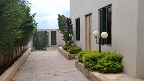 A stone pathway leading to a building with a green door and windows, surrounded by greenery and a lamp post. - Olerai Hotel (Kitengela)