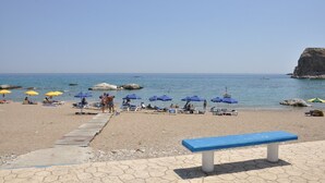 Une plage avec des chaises longues et des parasols, une promenade en bois et, au loin, une falaise rocheuse.
