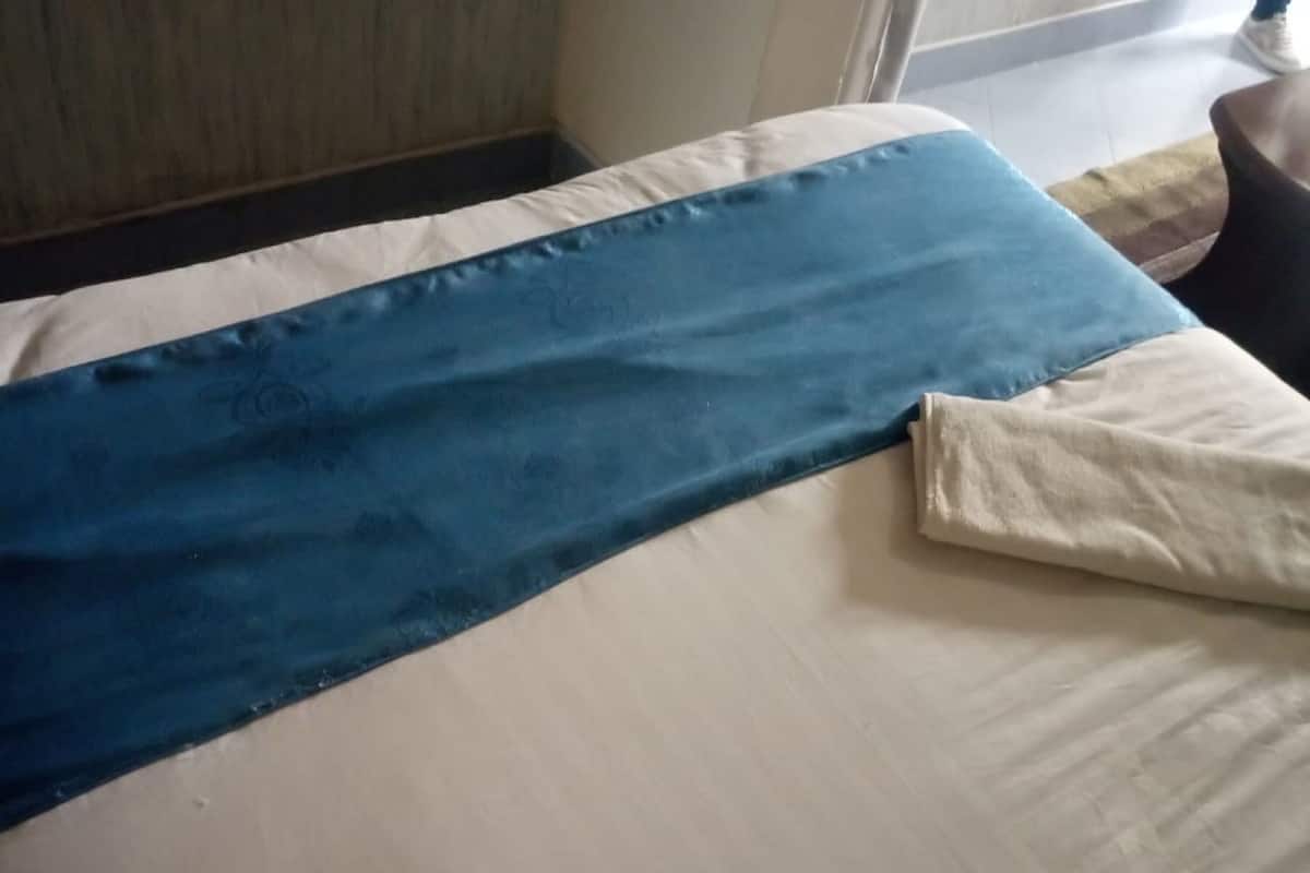 A bed with a blue and white bedspread, a beige pillow, and a folded beige blanket on the floor.