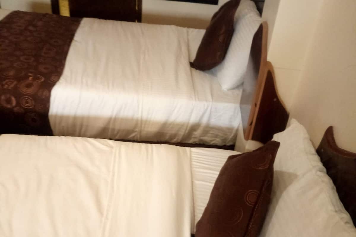 Two beds with white and brown bedding, wooden headboards, and a plain wall in the background.