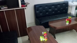 A room with a dark-colored sofa, a wooden coffee table with a bottle and a glass, and a wooden cabinet. - Remiz Guest House (Nakuru)