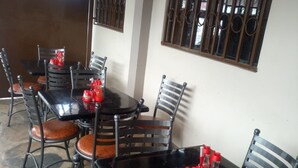 A dining area with tables and chairs, a tiled floor, and a window with bars. - Remiz Guest House (Nakuru)